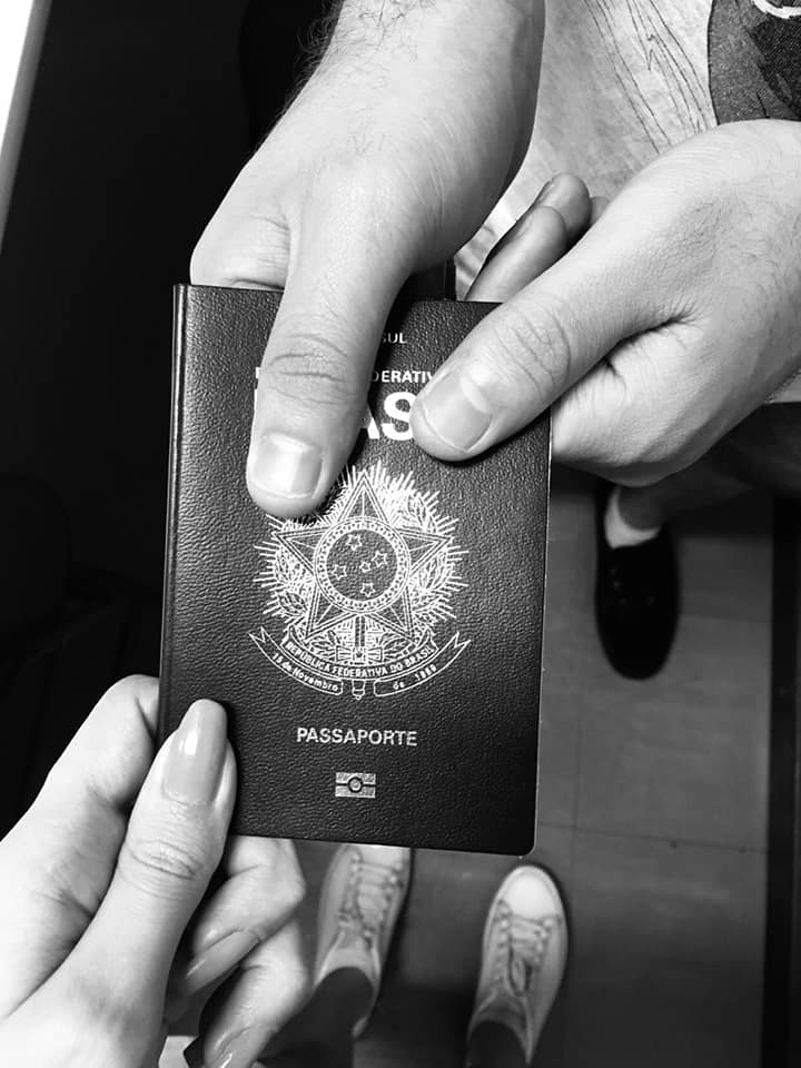 Imagem em preto branco de uma mão feminina e outra masculina segurando um passaporte.