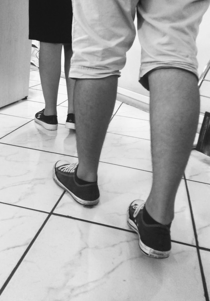 imagem da cintura para baixo de duas pessoas uma atrás da outra, ambas são brancas e estão de bermuda e tênis.