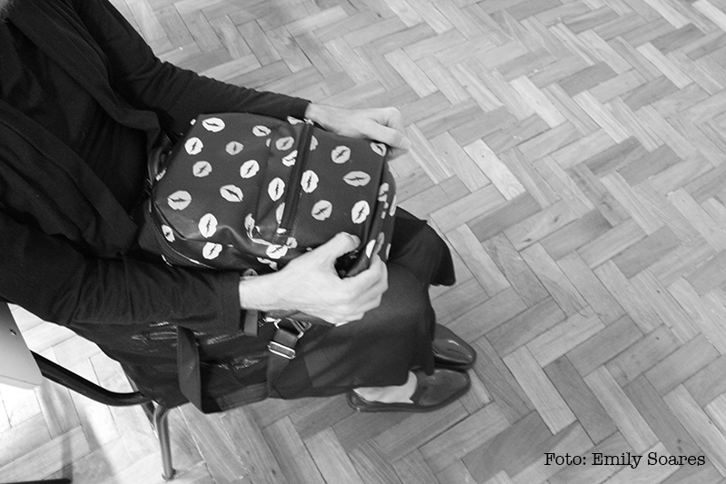 vemos uma menina sem rosto sentada, ela está segurando uma mochila pequena com força.