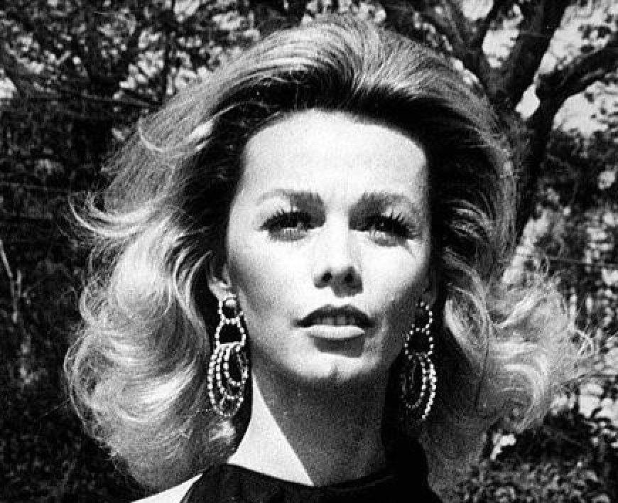 Uma imagem em preto e branco de uma mulher com um corte de cabelo volumoso e brincos grandes.