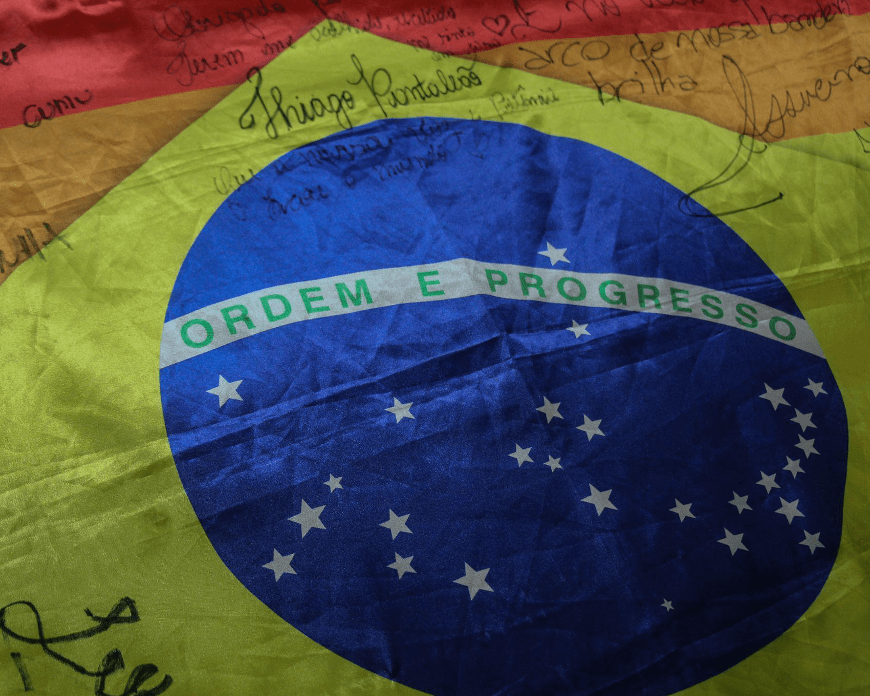 Bandeira do Brasil em close, com as cores do arco-íris, e nomes assinados em cima.