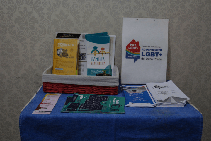 Mesa com diversos folhetos informativos sobre saúde, prevenção e direitos da comunidade LGBTQIAPN+. 