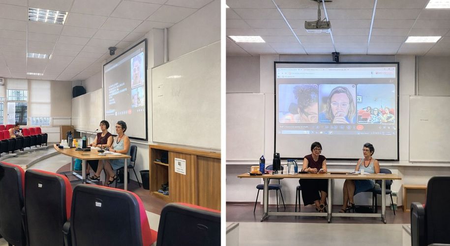 Duas mulheres sentadas em cadeiras em um auditório, à frente de uma tela de projetor.